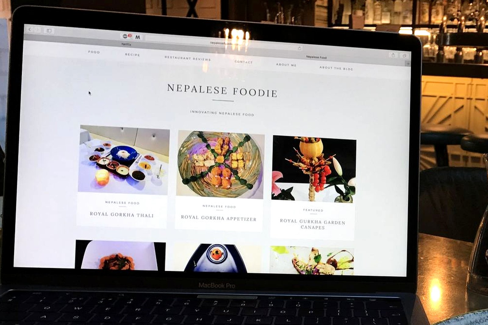 The 2017 Nepalese Foodie website open on a laptop screen in a bar, its dish titles legible.